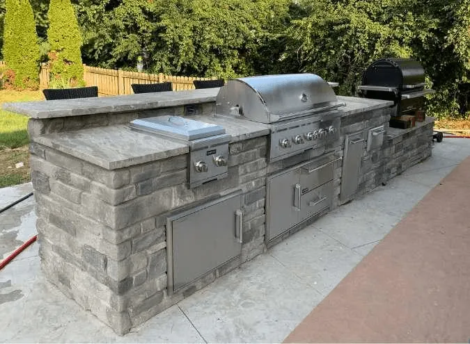 Modern outdoor kitchen installation with built-in grill, stone countertops, and bar area