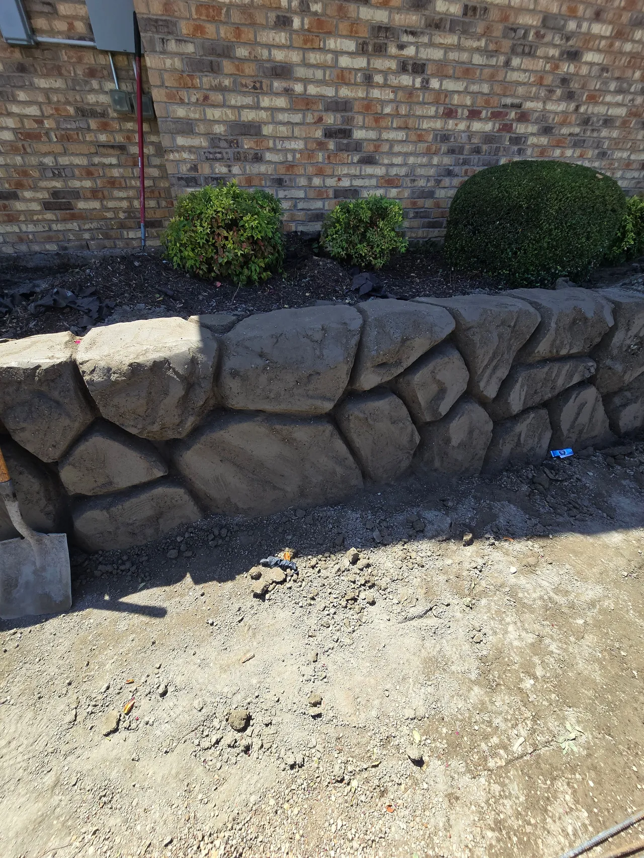Finished hand-carved concrete boulder retaining wall that replaced a railroad tie wall, holding a planting bed in Burleson TX