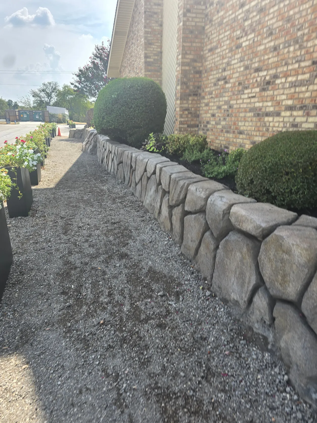 Hand-carved concrete boulder retaining wall holding a raised planter bed beside a gravel walk