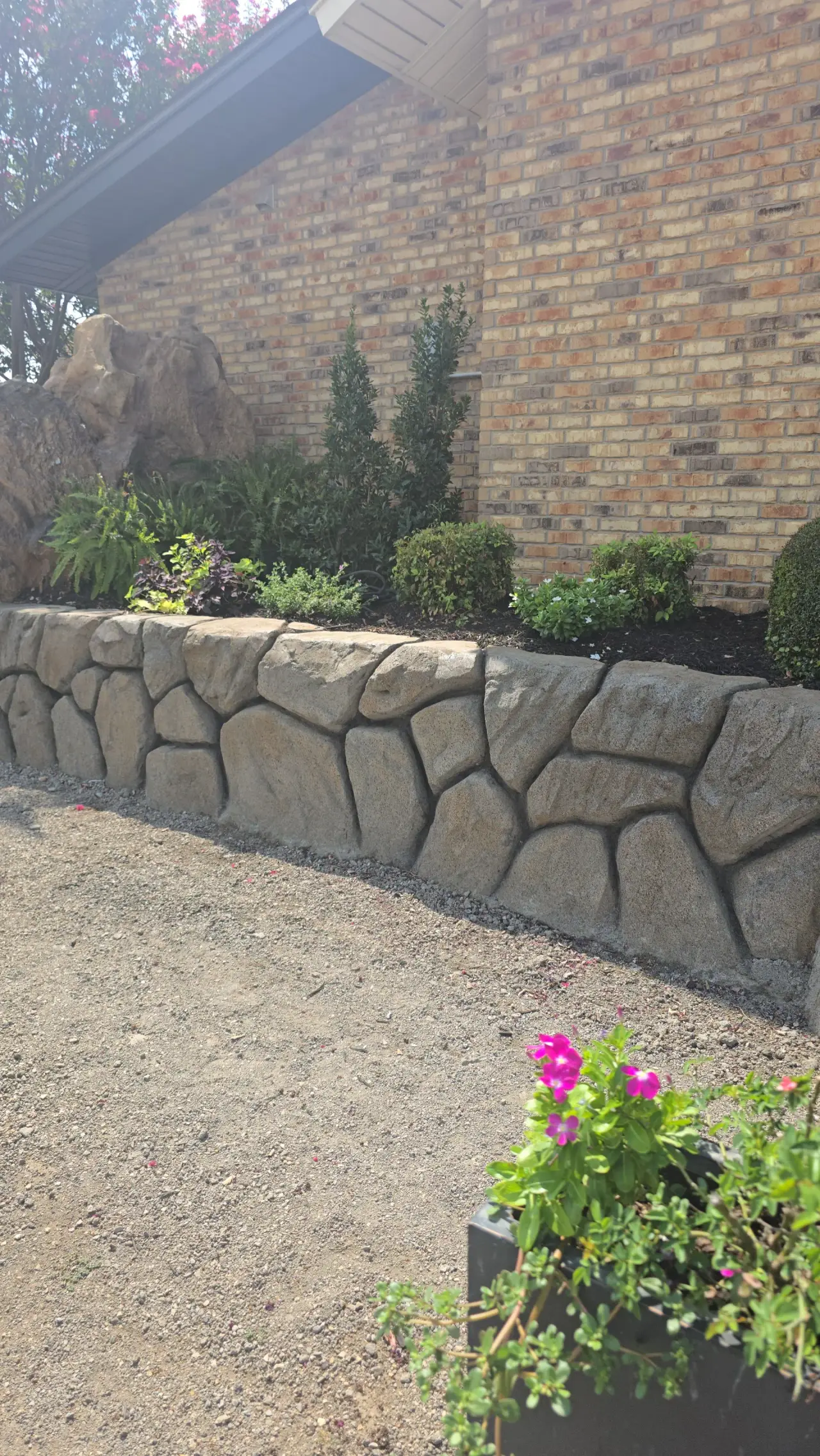 Hand-carved concrete retaining wall with a boulder-style face holding a raised planting bed against a brick wall