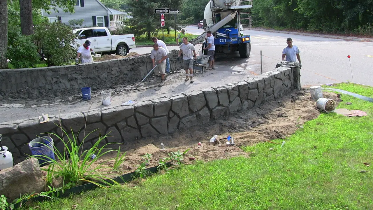 Crew hand-carving a stone pattern into a freshly poured concrete retaining wall