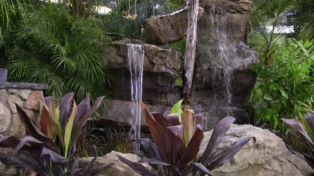 Hand-carved concrete rock waterfall with two water sheets falling between planted beds