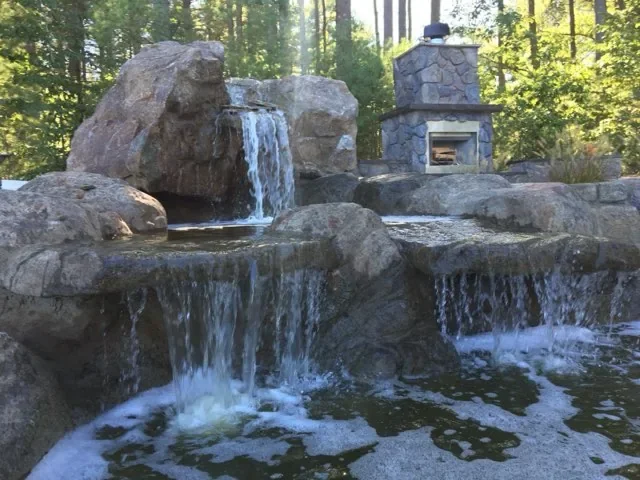 Hand-carved rock waterfall dropping in tiers into a pond, the kind of multi-tier feature we build on Westlake estate lots