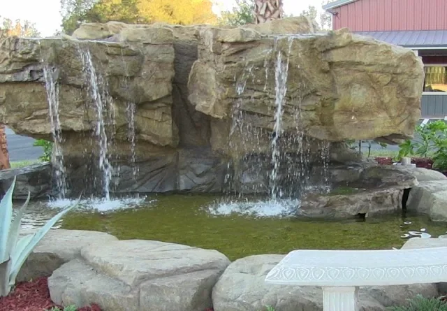 Hand-carved concrete rock waterfall spilling from several spouts into a pond, the kind of carved rock face we build for Northlake yards